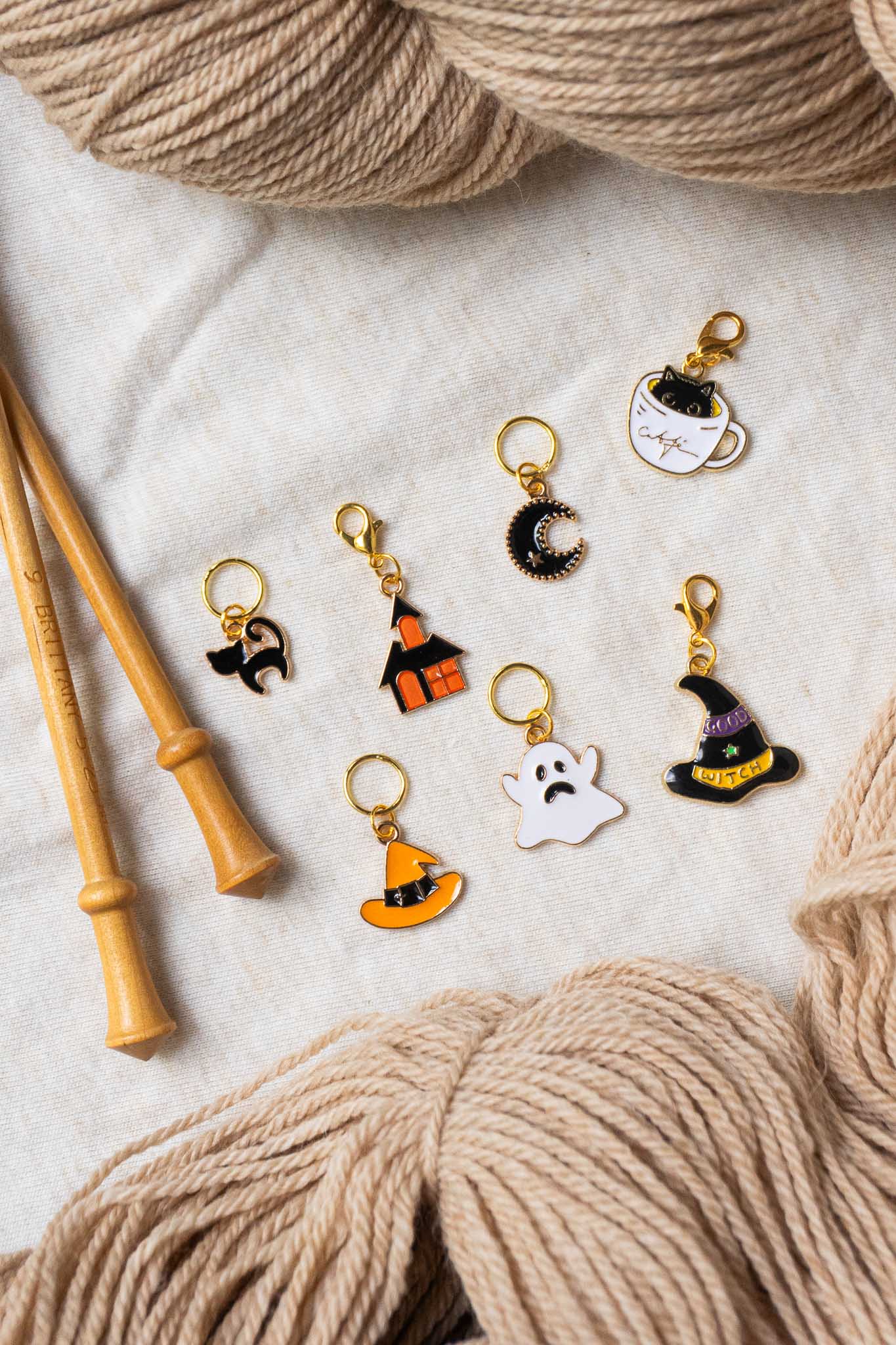 Set of Halloween-themed knitting stitch markers with yarn and knitting needles on a textured surface.