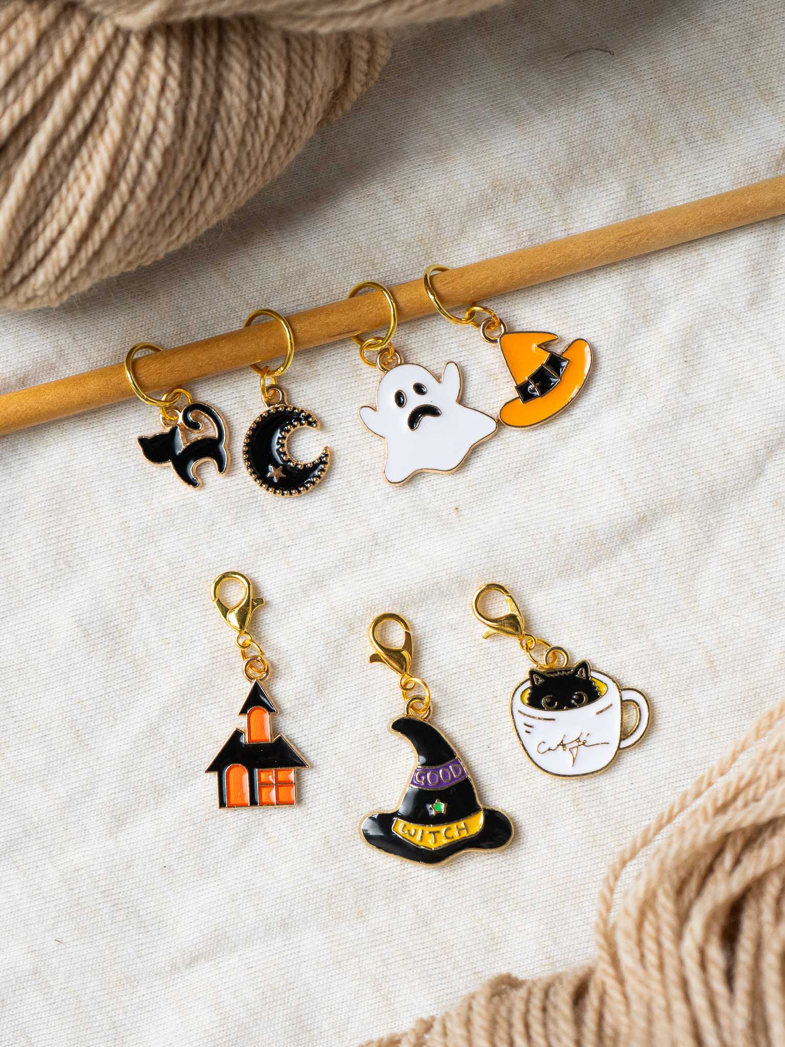 Set of Halloween-themed knitting stitch markers on a wooden needle with yarn in the background.